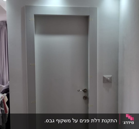 דלת לבנה עם ידית כסופה בקיר לבן